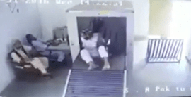 The traveler emerges from the other side of the baggage scanner, holding his bag, having ridden through it.