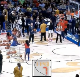Will in free throw position, holding a basketball as a lady passes him balls in the middle of a live contest.