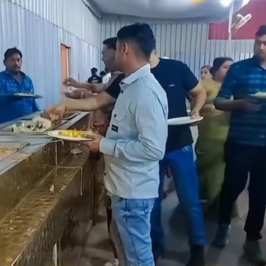 A man at a buffet, focused as he takes food with his left hand while his right hand holds the plate close to his body.