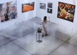 A woman taking pictures while walking backward in a museum, just before hitting a jar.