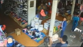 A shop owner reaches out to steady the fallen mannequin amid market stalls.
