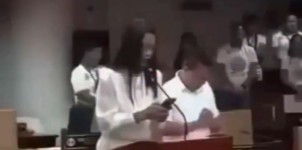 City councilor Grace Arago standing at the podium, reading from her phone during the opening prayer of a Tuguegarao council session.