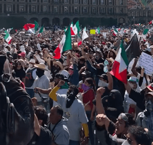 A crowd of protesters stands on one side of a street holding candles and signs, while a line of police in helmets and shields face them from the opposite side.