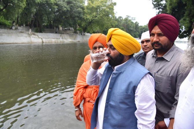 Bhagwant Mann holding a glass of water taken directly from the Kali Bein rivulet during a public event, surrounded by officials and media cameras.