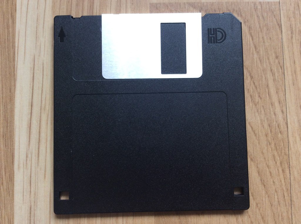 A close-up photo of a black 3.5-inch floppy disk on a wooden surface.