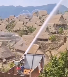 Automated water cannons spraying mist over traditional thatched-roof houses in Wengding village, Yunnan, during a fire-prevention system test.