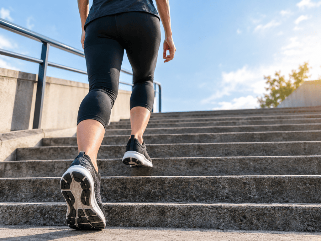 Person wearing running shoes climbing concrete stairs in daylight, illustrating the history of the 10,000-step walking target.